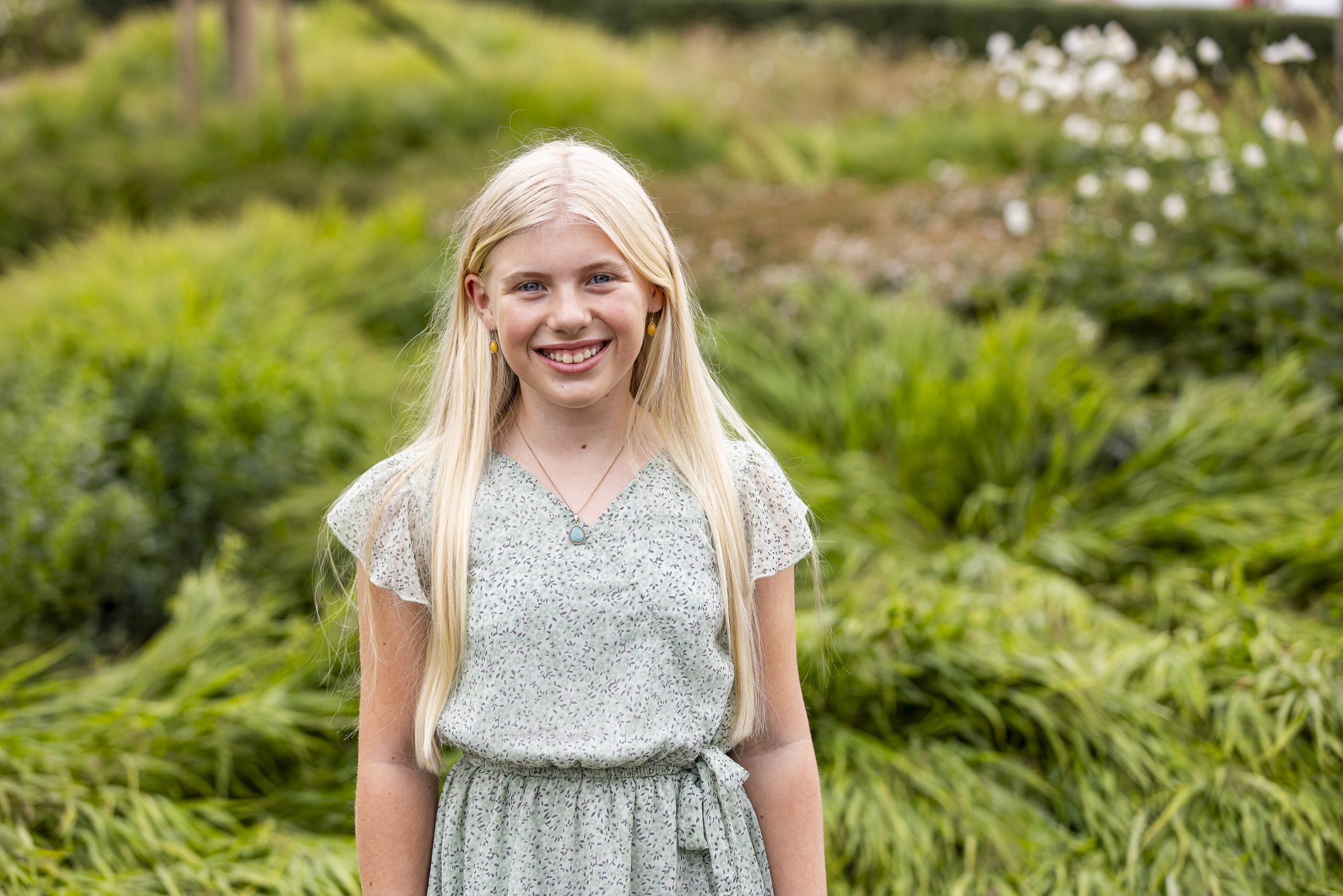 meisje met grote glimlach en lange blonde haren staat voor een groenperk